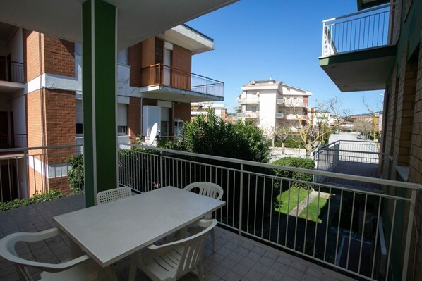 A balcony with a table and chairs, a view of neighboring buildings, and a clear sky.