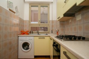 A compact kitchen with a washing machine, a stove, and a window with a view of the outside. - M027 - Marcelli, three-room apartment with terrace 150 meters from the sea (Marcelli)