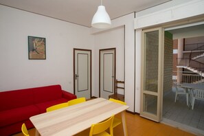 A room with a red sofa, a wooden table with yellow chairs, a white pendant light, and a sliding glass door leading to a balcony. - M027 - Marcelli, three-room apartment with terrace 150 meters from the sea (Marcelli)