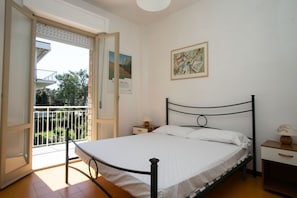 A bedroom with a bed, a nightstand, a lamp, and a balcony door.