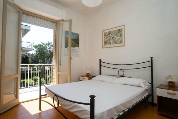 A bedroom with a bed, a nightstand, a lamp, and a balcony door.