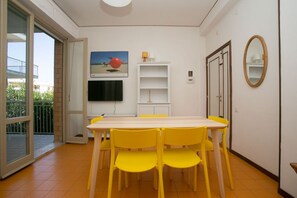 A dining area with a table and chairs, a television mounted on the wall, and a sliding glass door leading to an outdoor balcony.