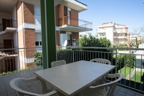A balcony with a table and chairs, a green pillar, and a view of neighboring buildings.