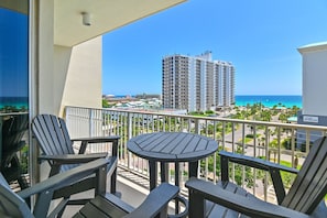 Un balcone con poltrone Adirondack e un tavolino rotondo, con vista su una spiaggia e un alto edificio di un albergo.