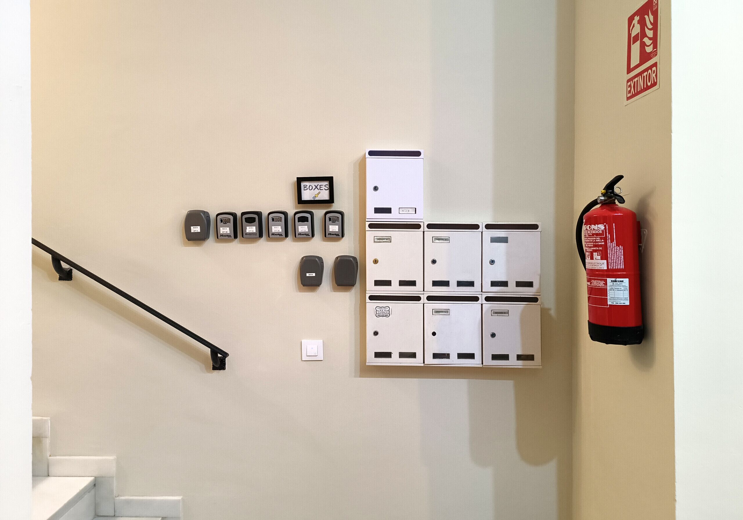 Un sistema di allarme incendio a parete, un estintore e un gruppo di citofoni.