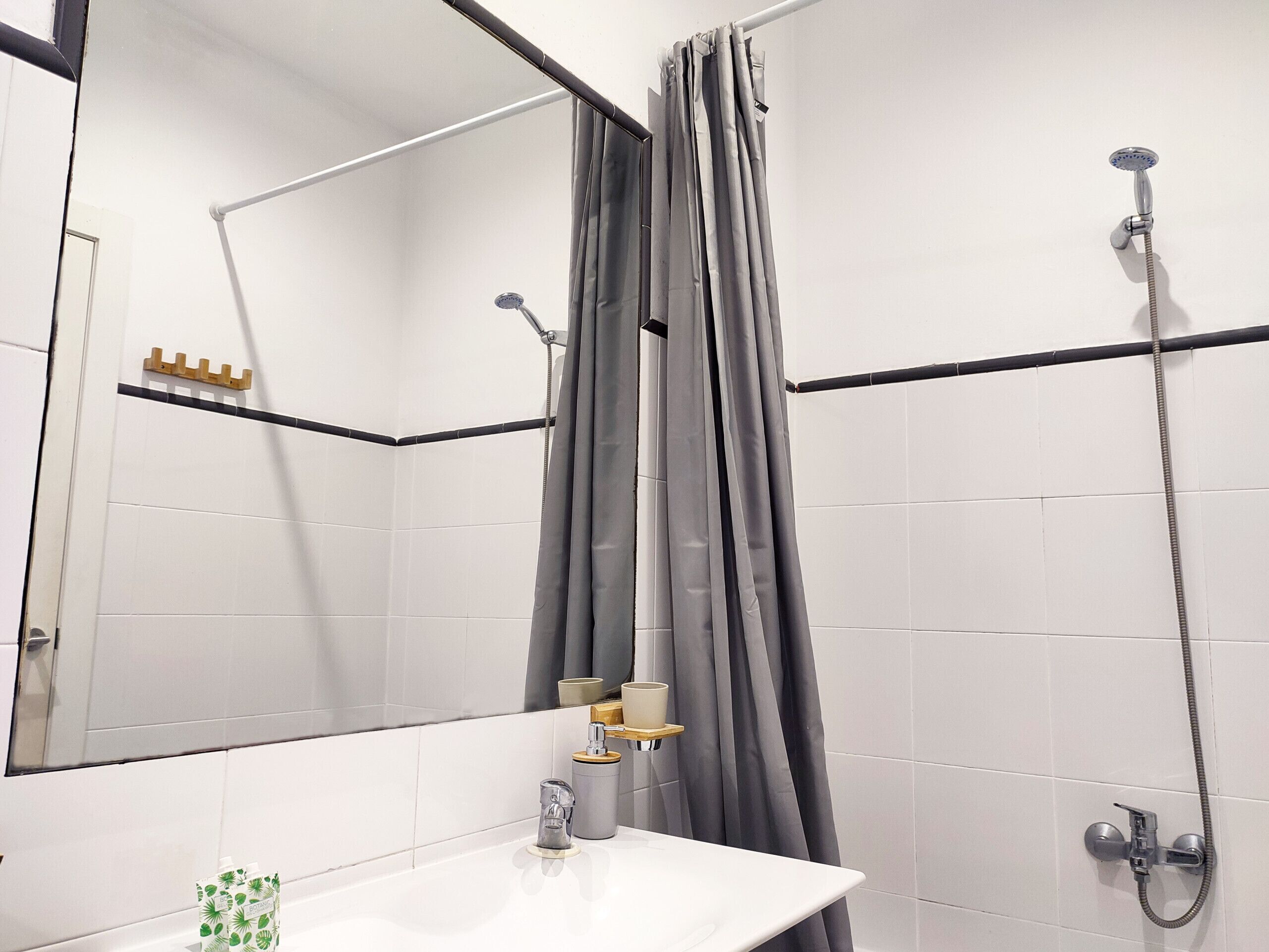 A bathroom with a white sink, a mirror, a shower with a handheld showerhead, and a curtain.