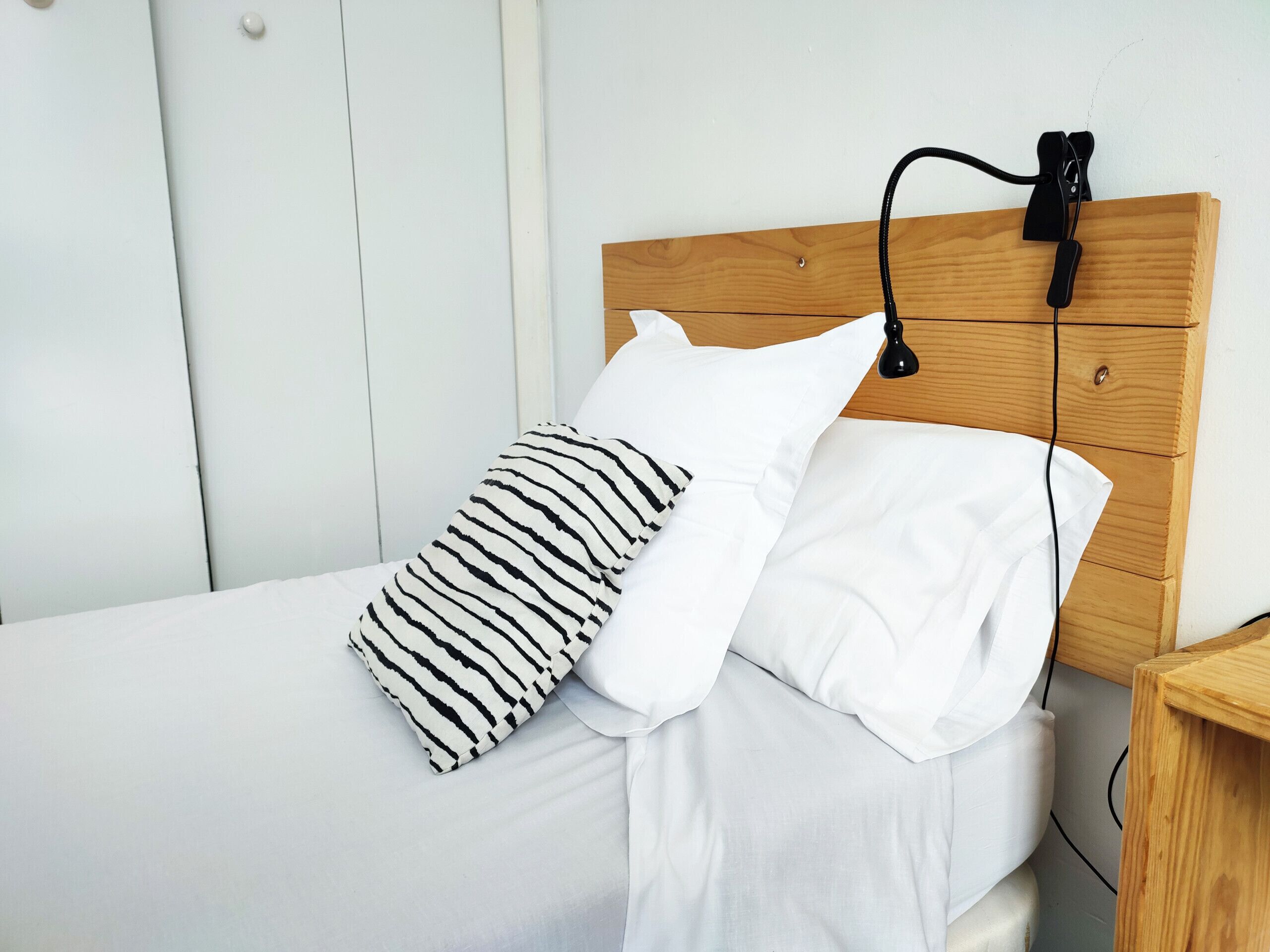 Ein Bett mit weißer Bettwäsche, einem gestreiften Kopfkissen und einem schlichten Kopfkissen.