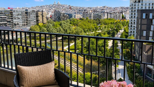 A balcony with wicker furniture, a view of a cityscape, and a river. - L'appartement Rostro (Paris)