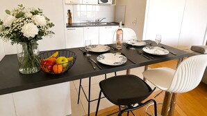A modern kitchen with white cabinets, a dining table set with plates, glasses, and cutlery, and a fruit bowl with apples and oranges. - L'appartement Rostro (Paris)