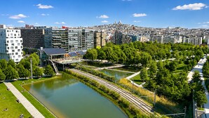 A riverside view of a cityscape with modern buildings, a park with a walking path, and a bridge. - L'appartement Rostro (Paris)