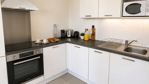 A modern kitchen with white cabinets, a stainless steel sink, a microwave, an oven, and a coffee maker. - L'appartement Rostro (Paris)