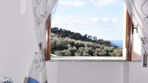 Una camera da letto con un letto, tende bianche con motivi neri e una finestra che si affaccia su una collina.
