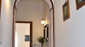 Un corridoio con pavimento decorato, un arco in legno, uno specchio a parete e un vaso con fiori.