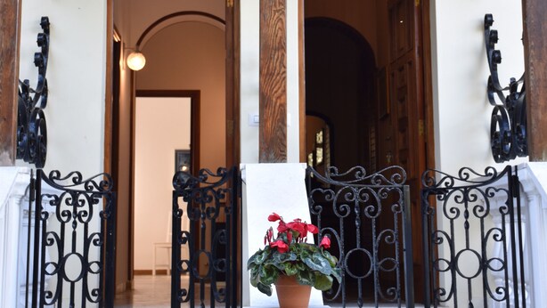 Un balcone in legno con ringhiere in metallo finemente decorate e una pianta in vaso.