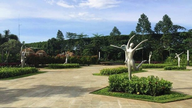 A spacious outdoor area with a central sculpture, surrounded by well-maintained greenery and a paved walkway. - Kelapa Gading House (Jakarta)