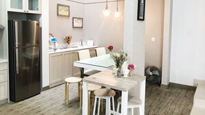 A modern kitchen with a stainless steel refrigerator, a dining table with white chairs, and pendant lights. - Kelapa Gading House (Jakarta)
