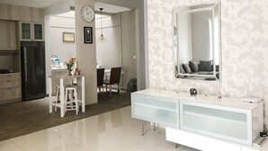 A modern kitchen with a refrigerator, a dining area with a table and chairs, and a bathroom with a large mirror and vanity. - Kelapa Gading House (Jakarta)