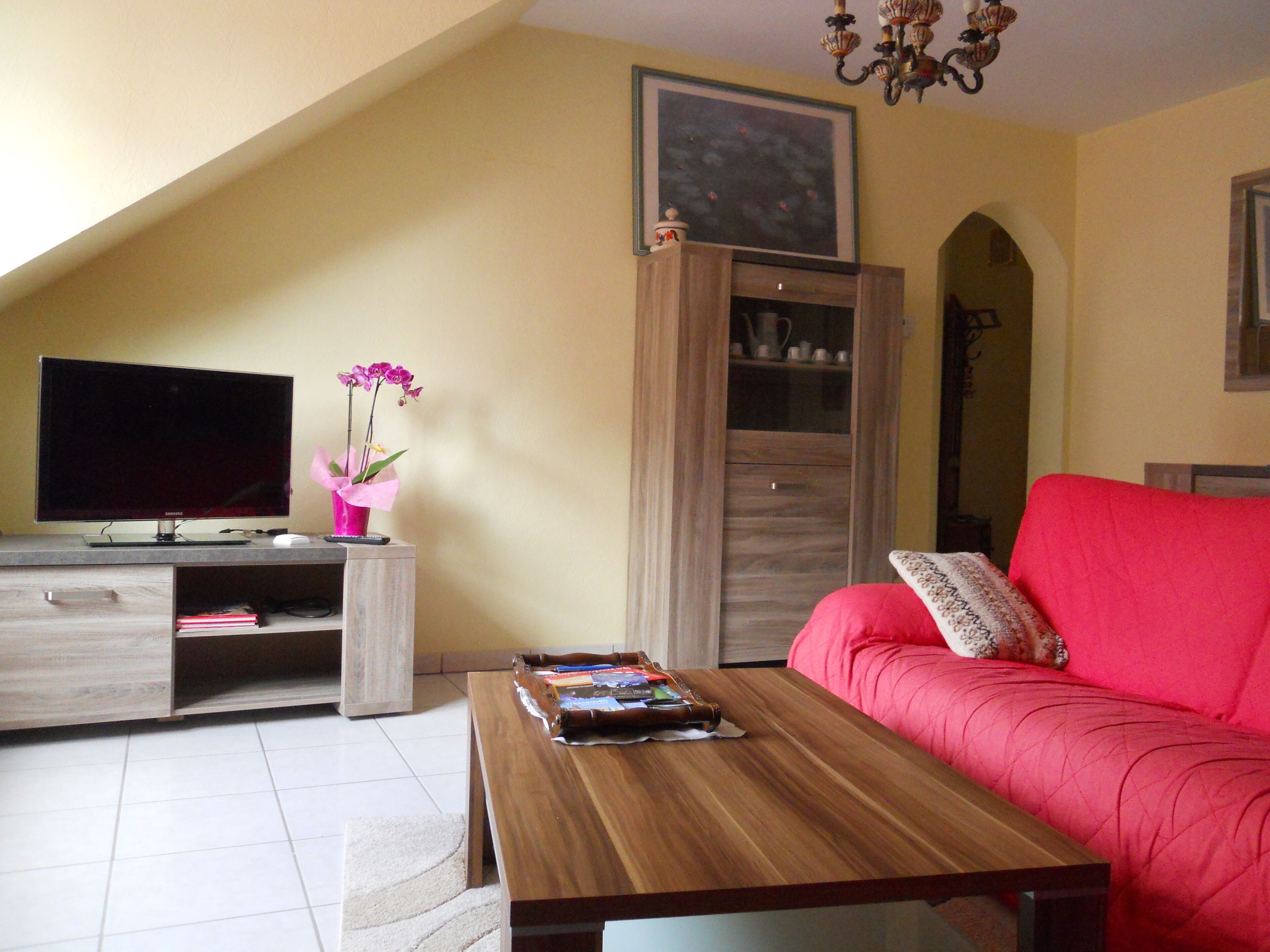 A living room with a television, a coffee table, a red sofa, and a cabinet.