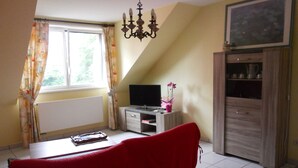 Una sala de estar con un sofá rojo, un televisor, un mueble y una ventana con cortinas.