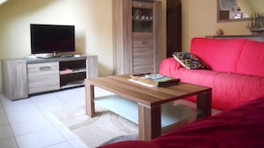 Una sala de estar con televisor, un mueble de madera, un sofá rojo y una mesita de centro.