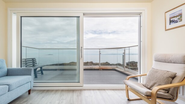 Una sala moderna con un ventanal corredizo que da a un balcón, un sofá azul claro y un sillón de madera con cojín.