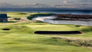Un campo de golf con búnkeres, una bandera y un edificio al fondo.