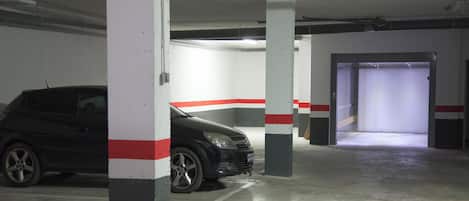 Un parking où une voiture noire est garée près d’un pilier.