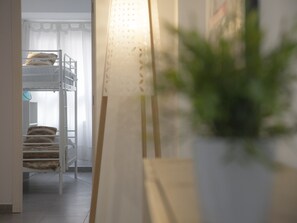 A bunk bed room with a white headboard, a potted plant, and a window with sheer curtains.