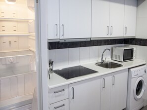 A compact kitchen with white cabinets, a microwave, a sink, and a washing machine.