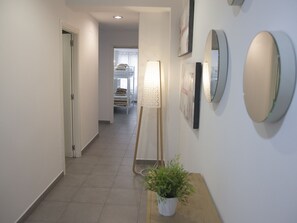 A hallway with a bed, a standing lamp, and a potted plant.