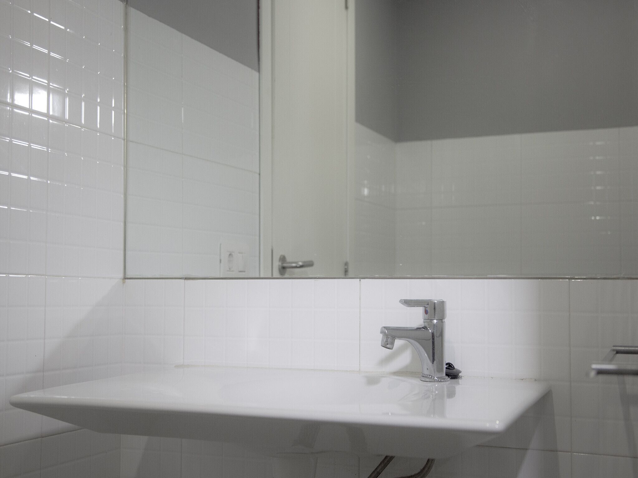 Une salle de bain avec un lavabo blanc, un miroir et des murs recouverts de carreaux blancs.