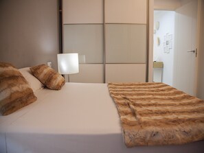 A neatly made bed with a striped blanket and two pillows, a bedside lamp, and a door leading to a bathroom with a mirror and a small table. - Flats Friends Tetuan 2 bedrooms (Valencia)