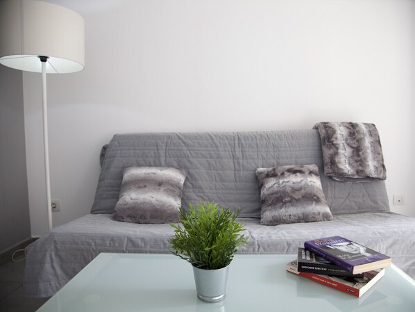 A modern living room with a grey sofa, a white lamp, and a glass coffee table with a potted plant and books.