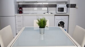 A modern kitchen with white cabinets, a microwave, a washing machine, and a glass table with a potted plant. - Flats Friends Tetuan 2 bedrooms (Valencia)