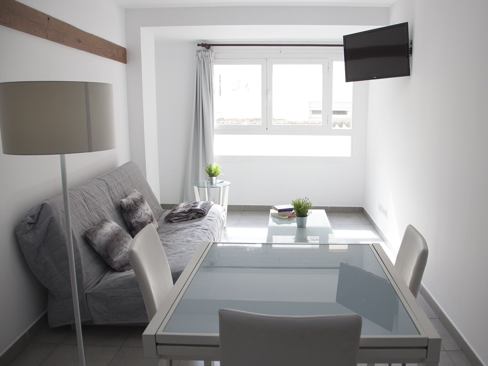 Una sala de estar moderna y minimalista con un sofá gris, una mesa de centro de vidrio y un televisor de pantalla plana montado en la pared.