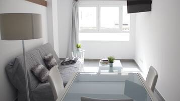 Una sala de estar moderna y minimalista con un sofá gris, una mesa de centro de vidrio y un televisor de pantalla plana montado en la pared.