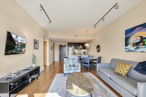 Ein modernes Wohnzimmer mit Sofa, Couchtisch und Essbereich. Im Hintergrund ist eine Küche mit Esstisch und Stühlen zu sehen.