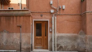 Un edificio con puerta de madera, una ventana pequeña y un contador de servicios en la pared.