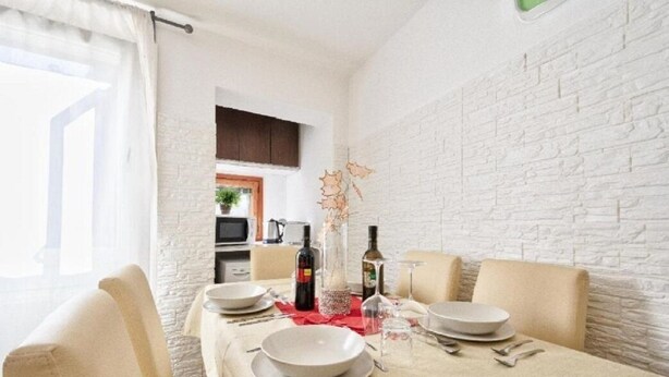 Un comedor con pared de ladrillo blanco, una mesa dispuesta con platos, vasos y cubiertos, y una ventana con cortinas.