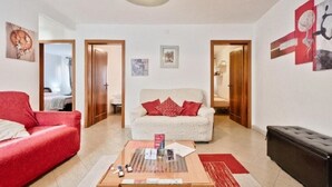 Una sala de estar con un sofá rojo, un sofá blanco con cojines rojos, una mesa de centro con revistas y un reposapiés negro.