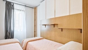 Una habitación de hotel con dos camas, un ventanal con cortinas y un cabecero de madera con repisa.