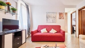 Una sala de estar con un sofá rojo, un televisor en un mueble y un cuadro en la pared.