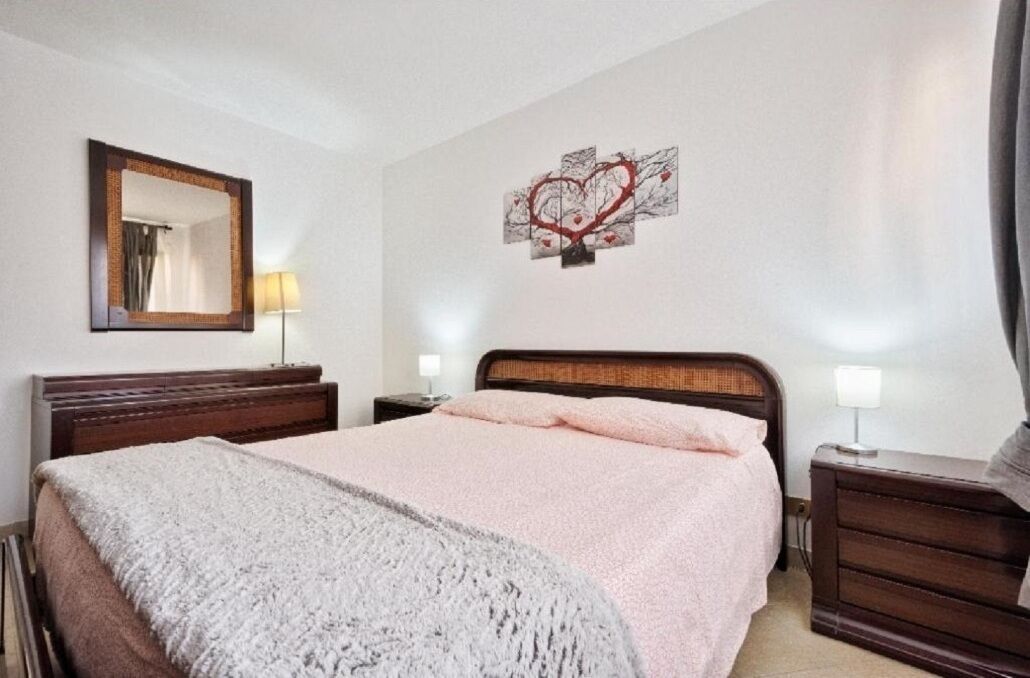 Ein Schlafzimmer mit einem Bett, einem Nachttisch, einer Kommode, einem Spiegel und einem Wandbild.