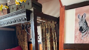 Ein gemütliches Zimmer mit einem Holzbett, einem kleinen Tisch mit Topfpflanze und einem Zebra-Gemälde an der Wand.