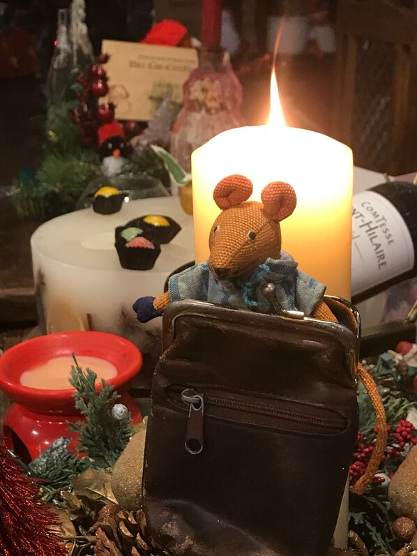 A small brown teddy bear sitting on a black backpack with a lit candle behind it.