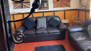 Ein Wohnzimmer mit einem schwarzen Ledersofa, einem gemusterten Zierkissen und einem kleinen Beistelltisch.