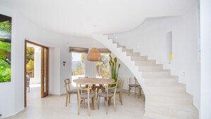 A spacious room with a round wooden table and chairs, a staircase with beige steps, and a large window offering a view of greenery. - Villa ROSINA by Abahana Villas (Benissa)