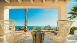 A terrace with two wicker chairs, a wooden table, and a view of the sea and a mountain. - Villa ROSINA by Abahana Villas (Benissa)