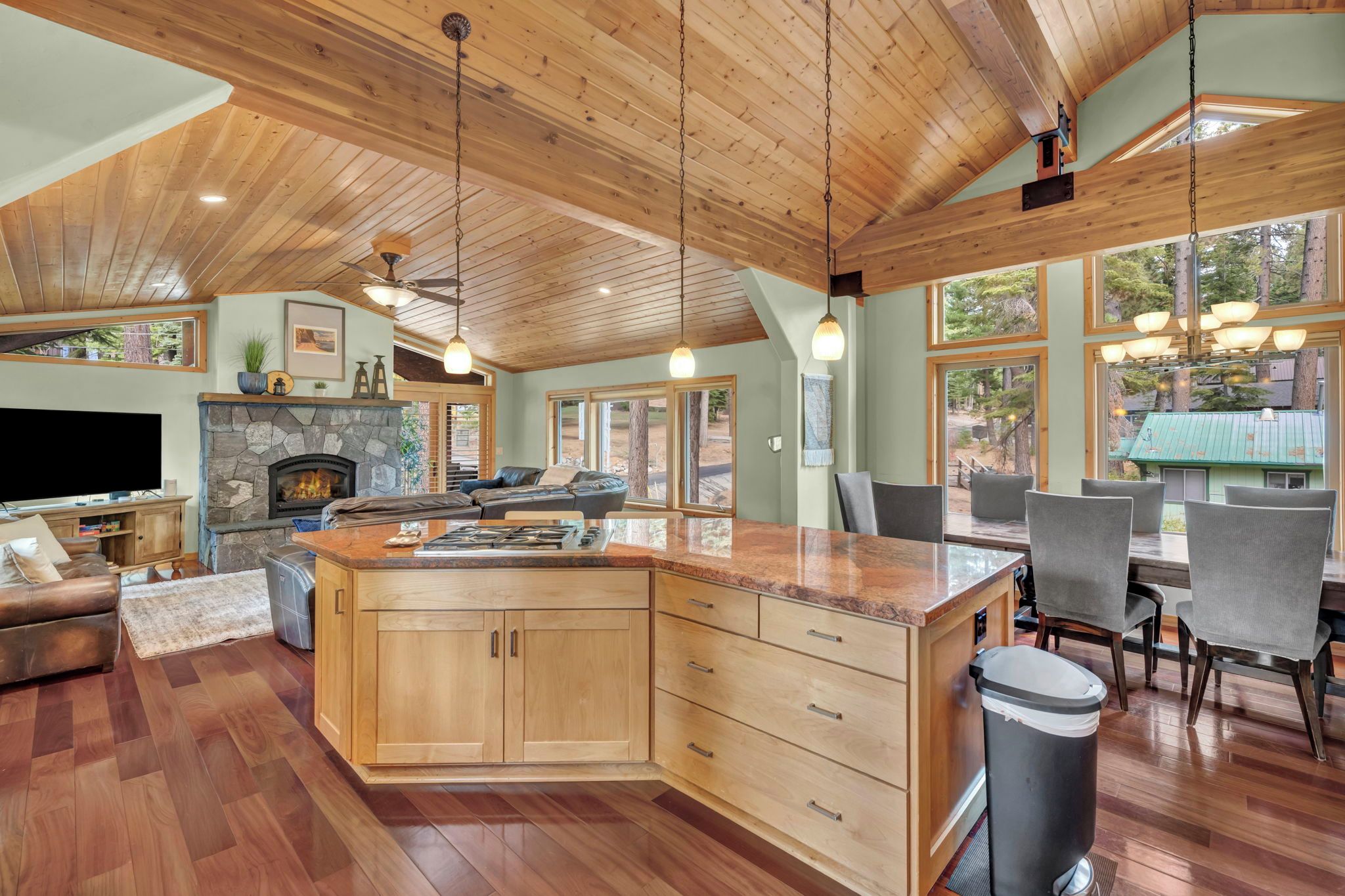 A spacious kitchen with a large island, wooden cabinetry, and a stone fireplace.