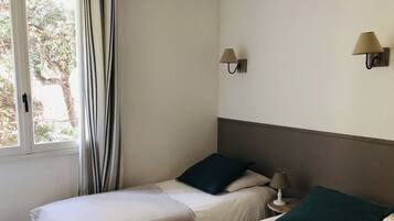 A hotel room with two beds, a window with curtains, and two wall-mounted lamps.